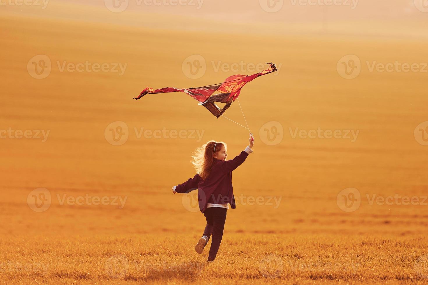 Happy little girl running with kite in hands on the beautiful field photo