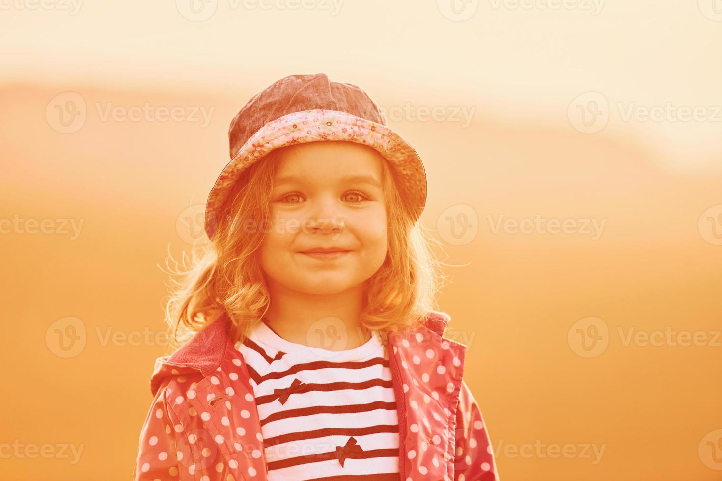 Portrait of cute little girl that standing outdoors illuminated by orange sunlight photo