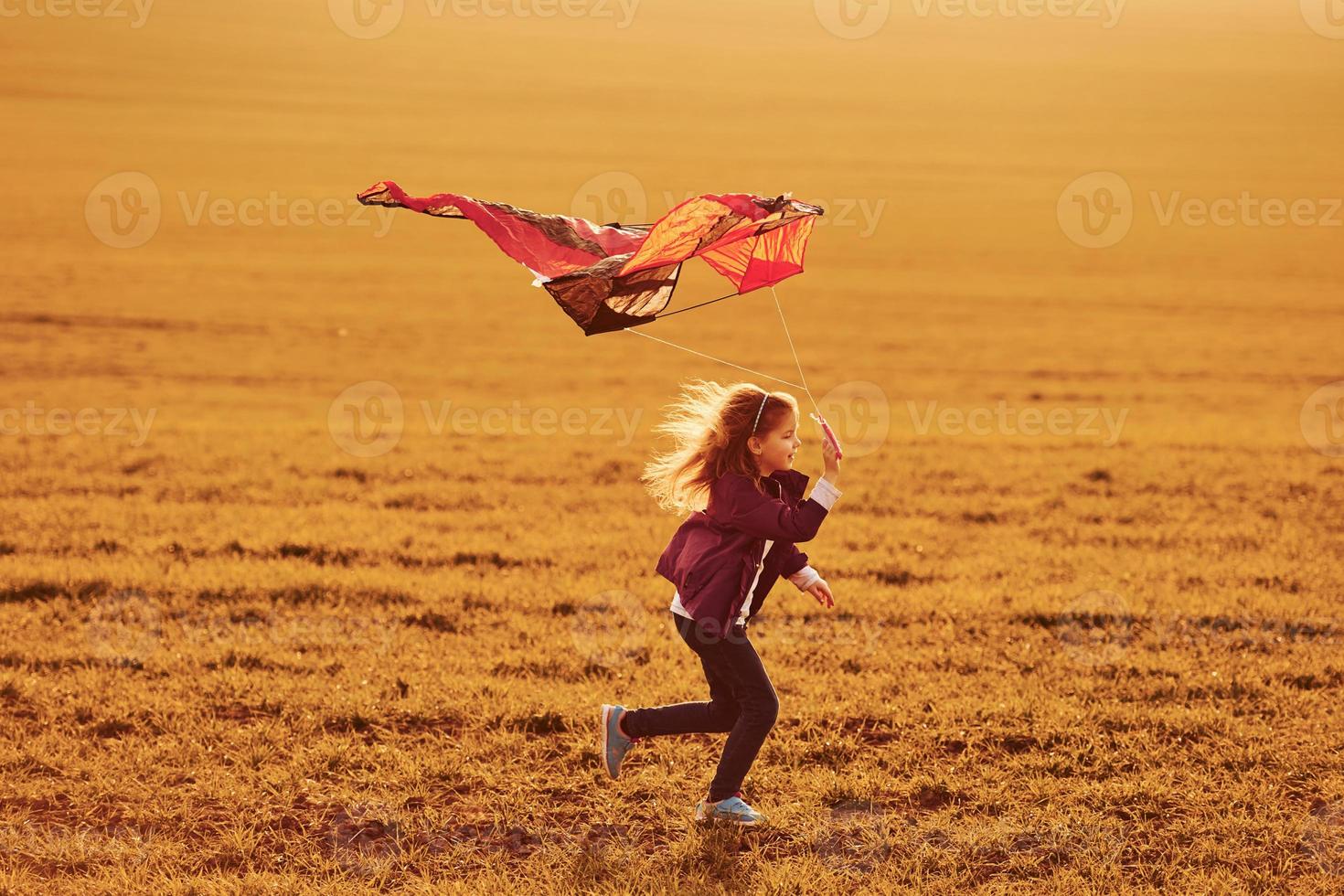 Happy little girl running with kite in hands on the beautiful field photo