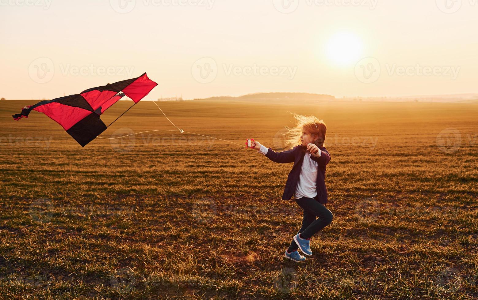 Happy little girl running with kite in hands on the beautiful field at sunrishe time photo
