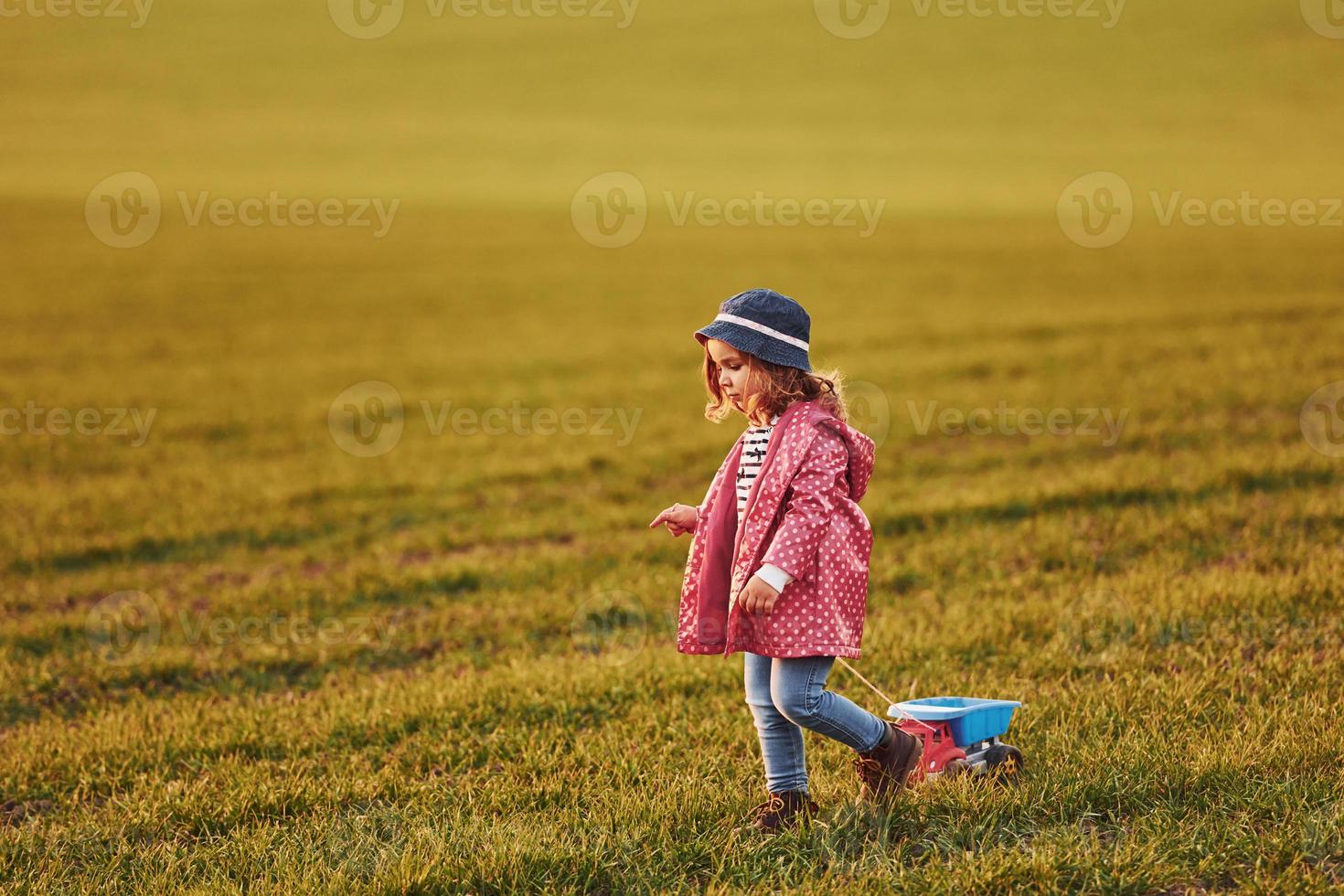 Cute little girl walks with toy car on the beautiful field at sunny daytime photo