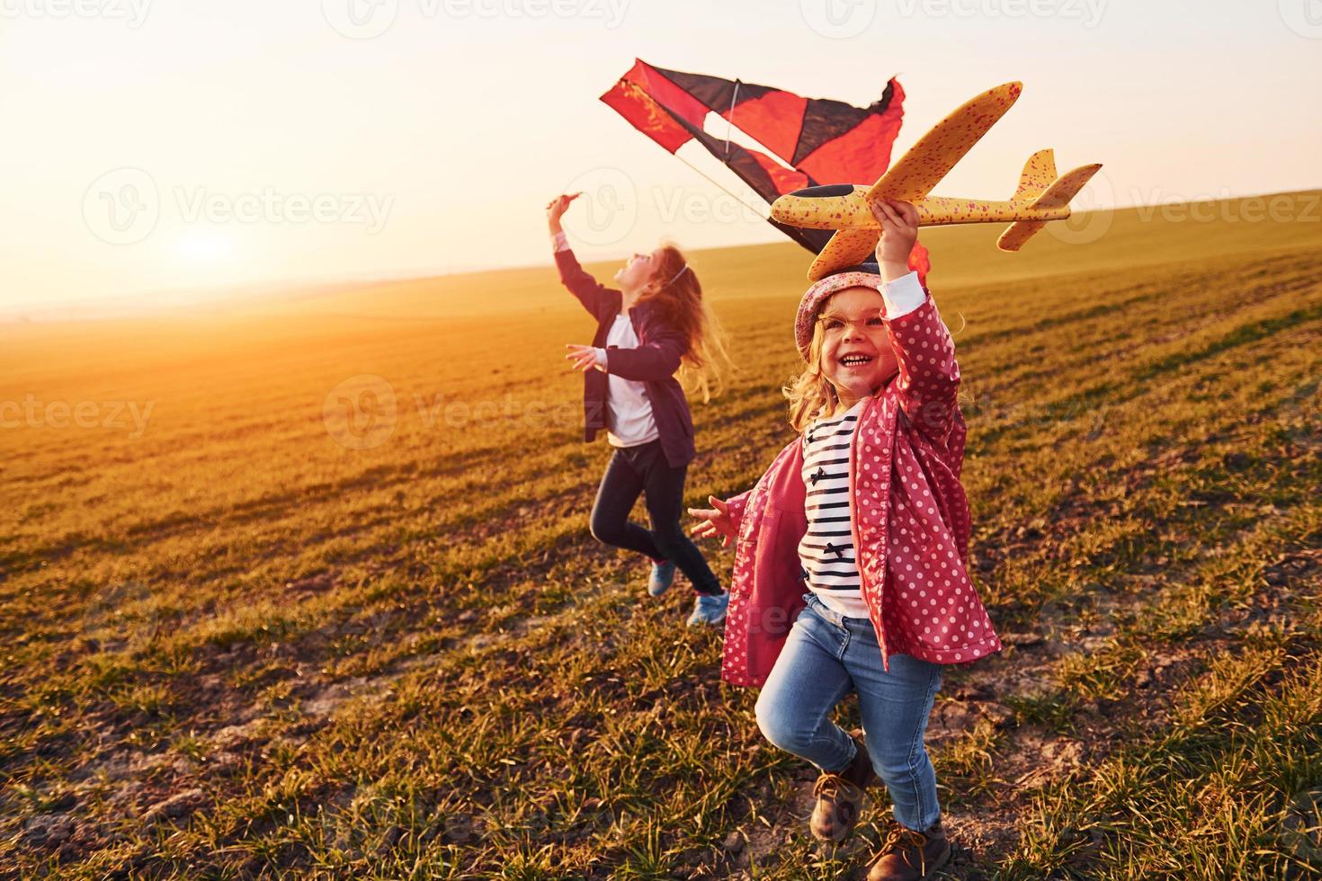 dos amigas se divierten juntas con cometas y aviones de juguete en el campo durante el día soleado foto