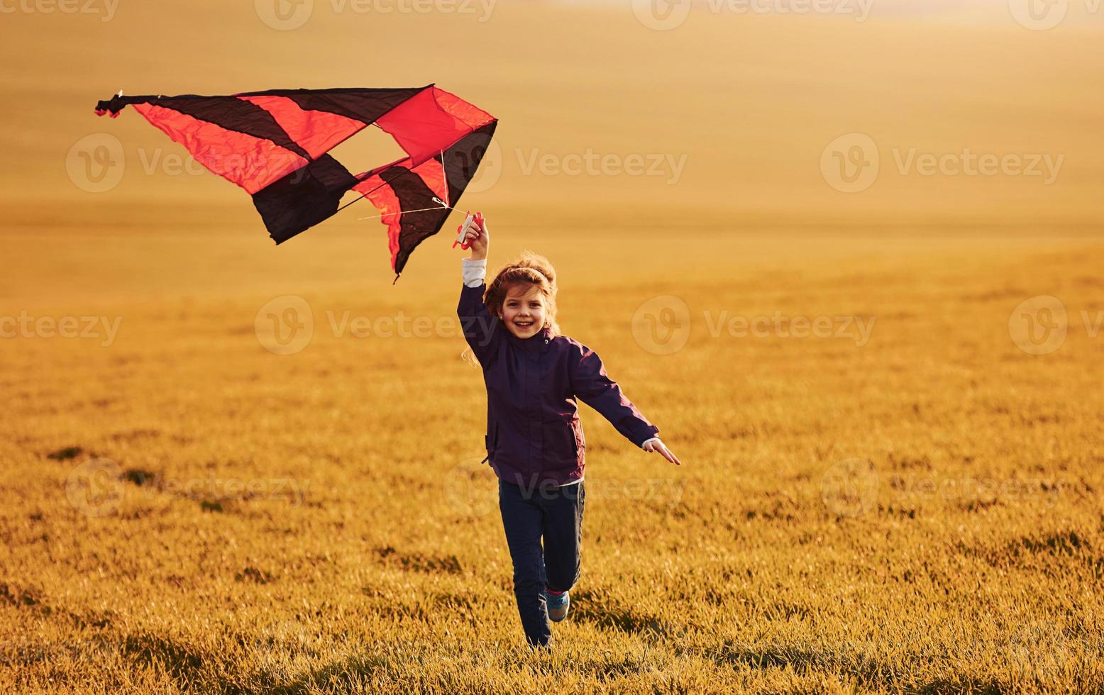 Happy little girl running with kite in hands on the beautiful field photo