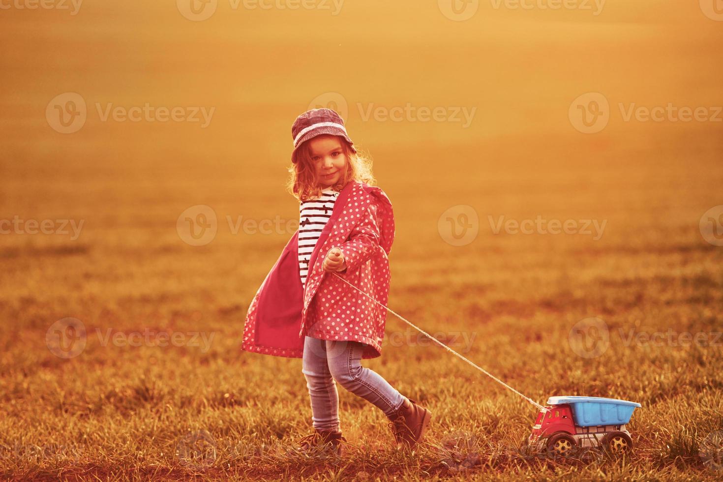 una linda niña camina con un camión de juguete en el hermoso campo durante el día soleado foto