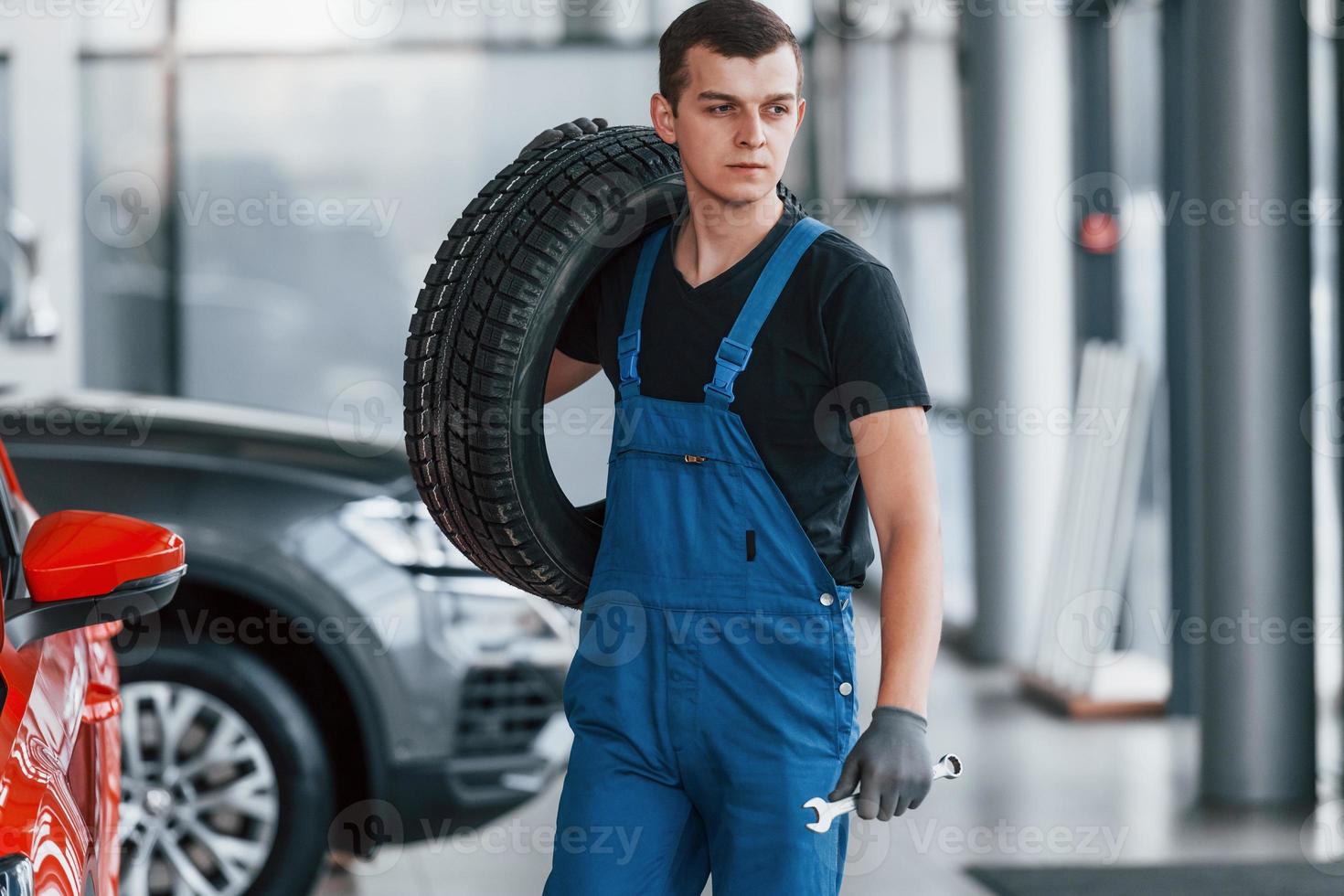 trabajador con uniforme negro y azul que sostiene la rueda del camión y tiene trabajo en el interior foto