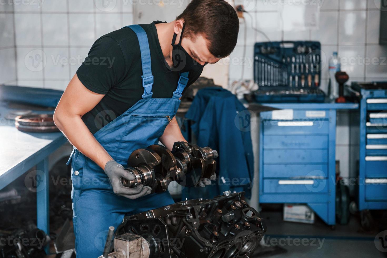 Professional repairman in black protective mask works with broken automobile engine photo