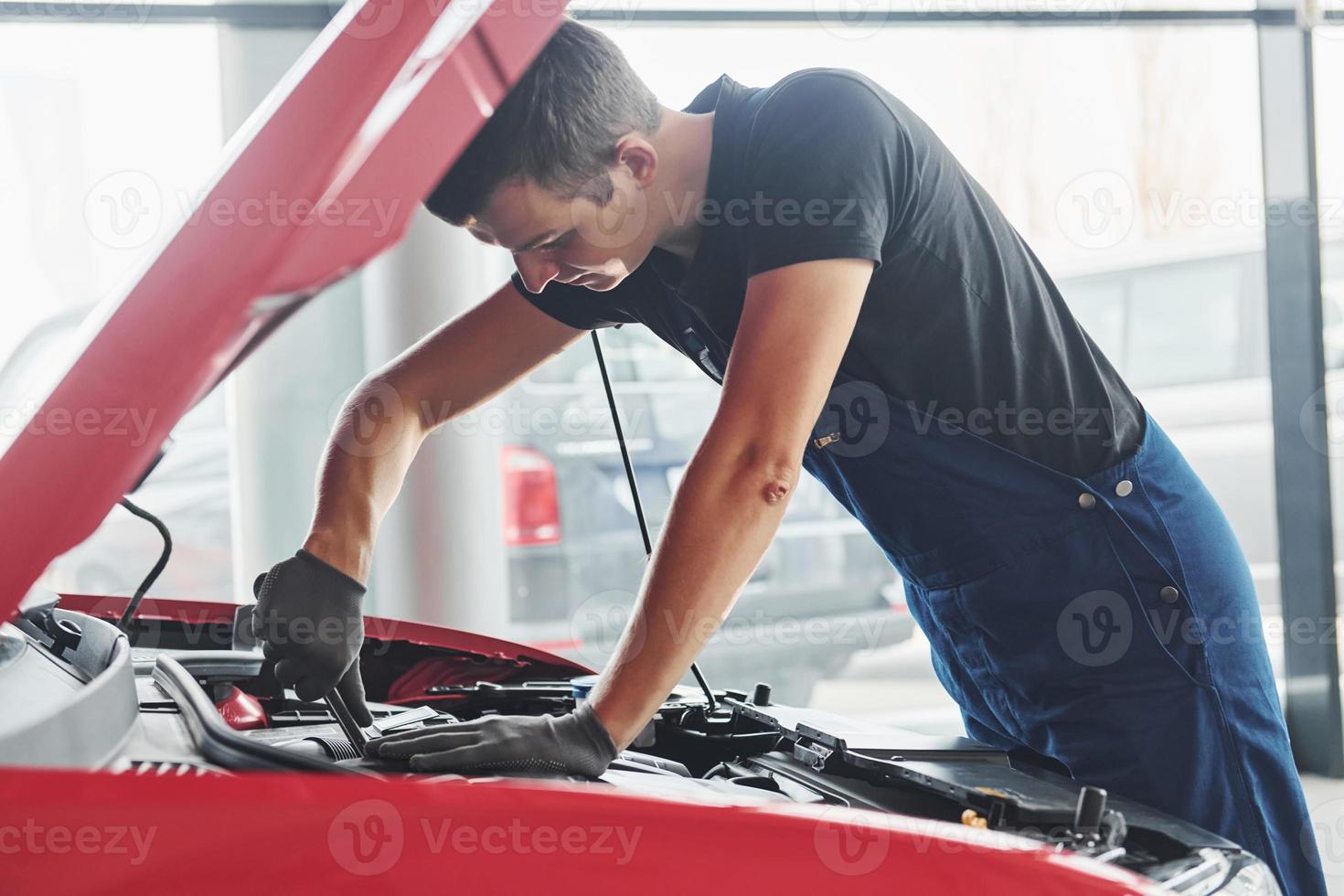 Man in uniform works with broken automobile. Conception of car service photo