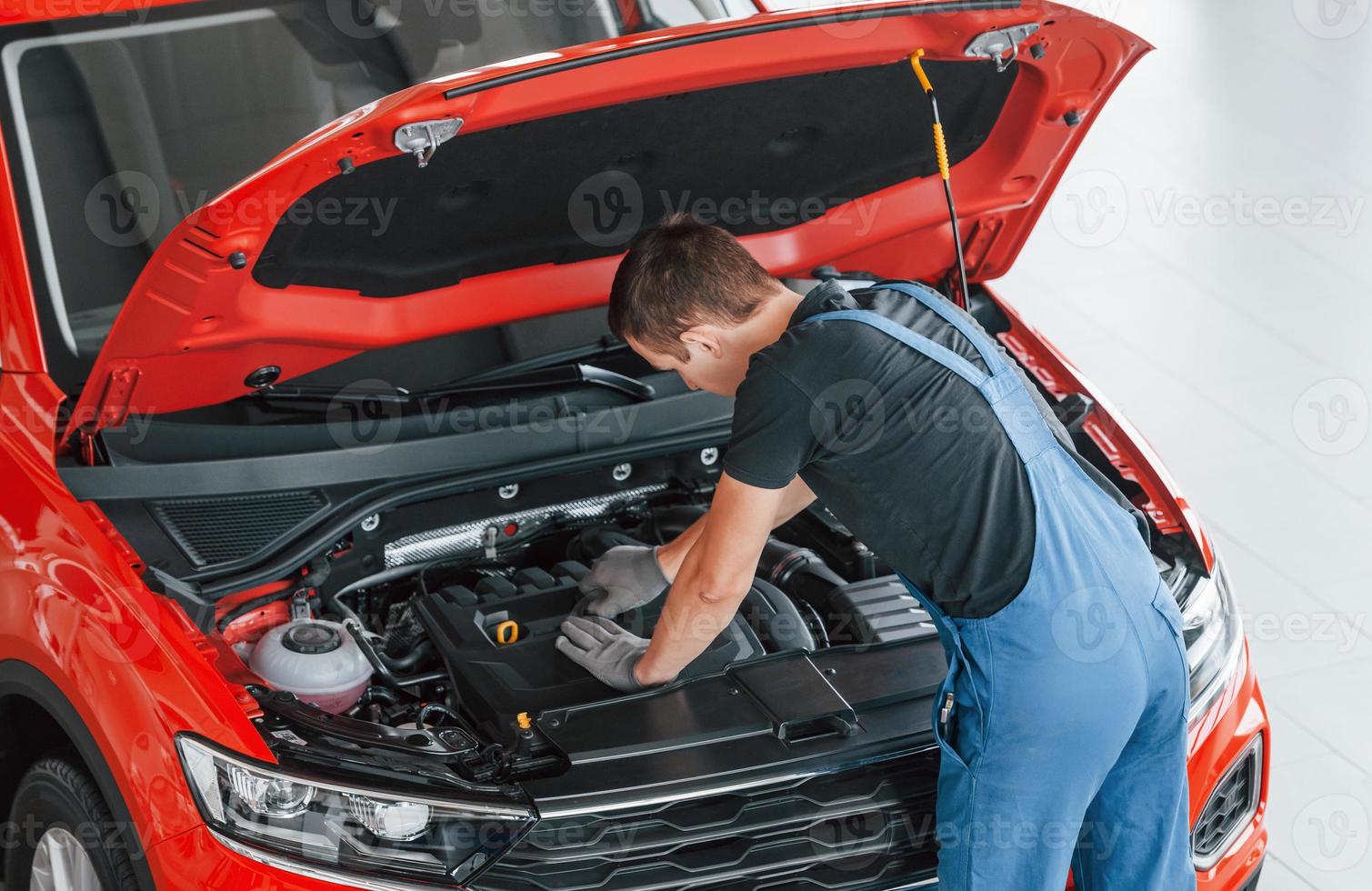 Top view of male worker in uniform that repairs red automobile photo