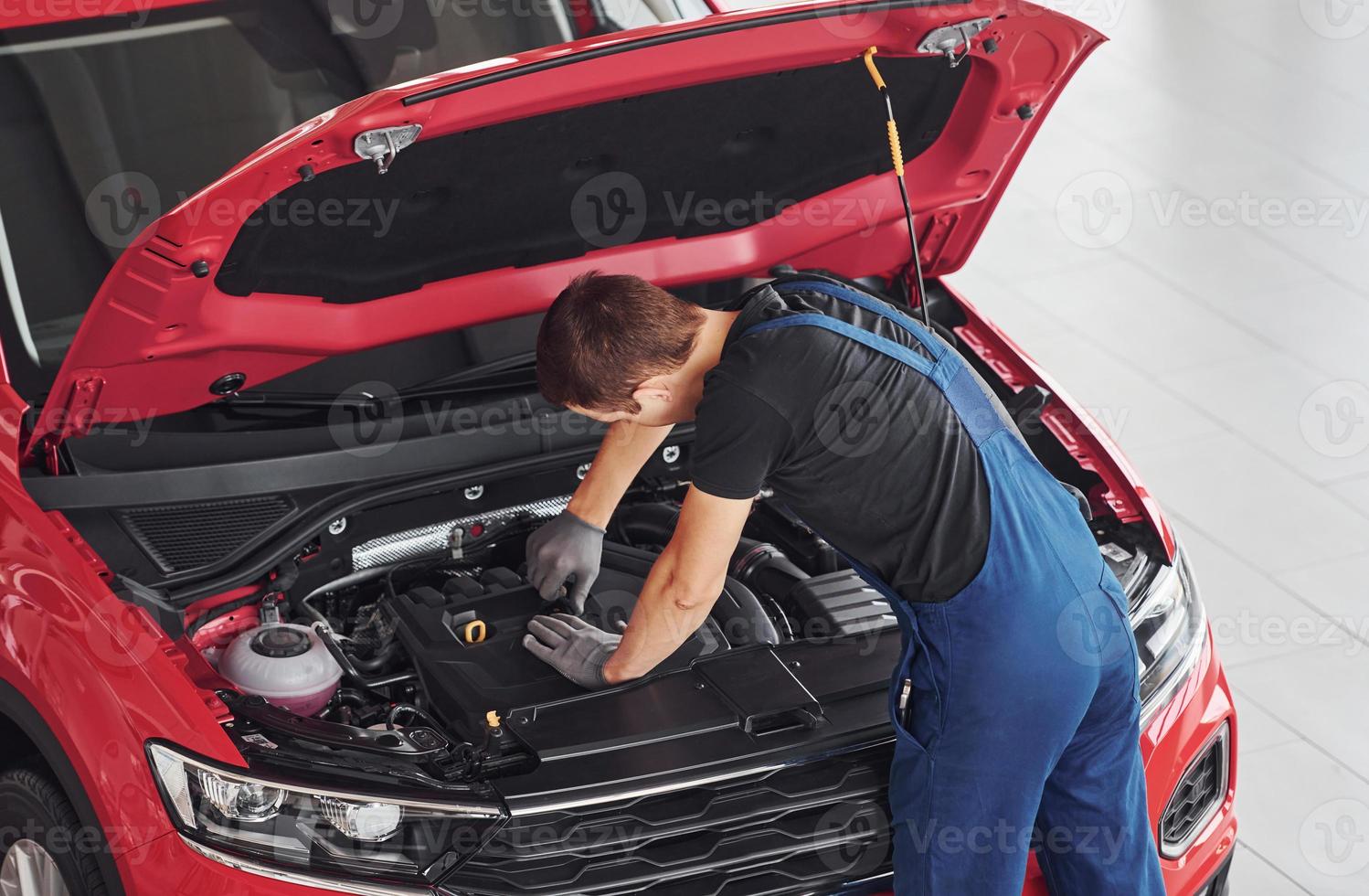 Top view of male worker in uniform that repairs red automobile photo