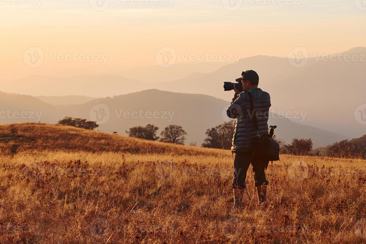 fotógrafo masculino de pie y trabajando en el majestuoso paisaje de árboles y montañas de otoño en el horizonte foto