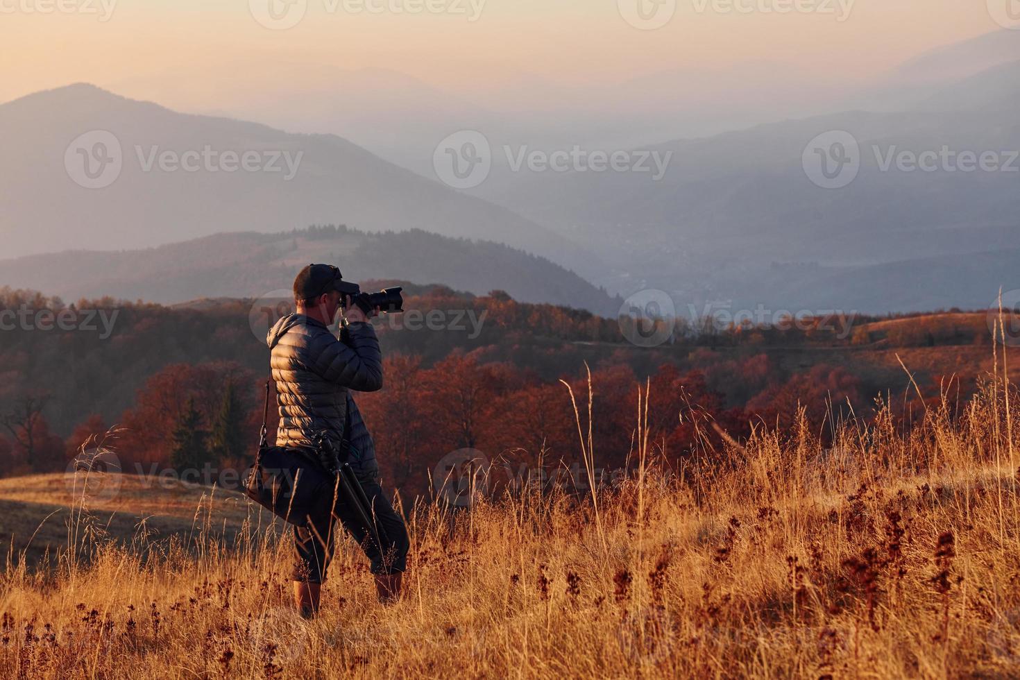 Male photographer standing and working at majestic landscape of autumn trees and mountains by the horizon photo