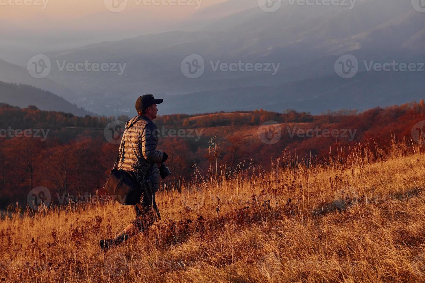 Male photographer standing and working at majestic landscape of autumn trees and mountains by the horizon photo