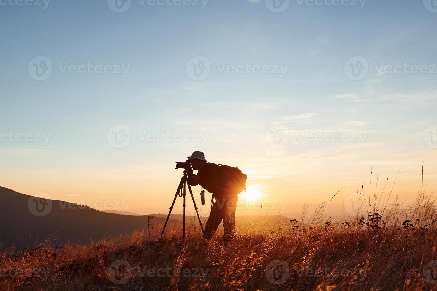 fotógrafo masculino de pie y trabajando en el majestuoso paisaje de árboles y montañas de otoño en el horizonte foto