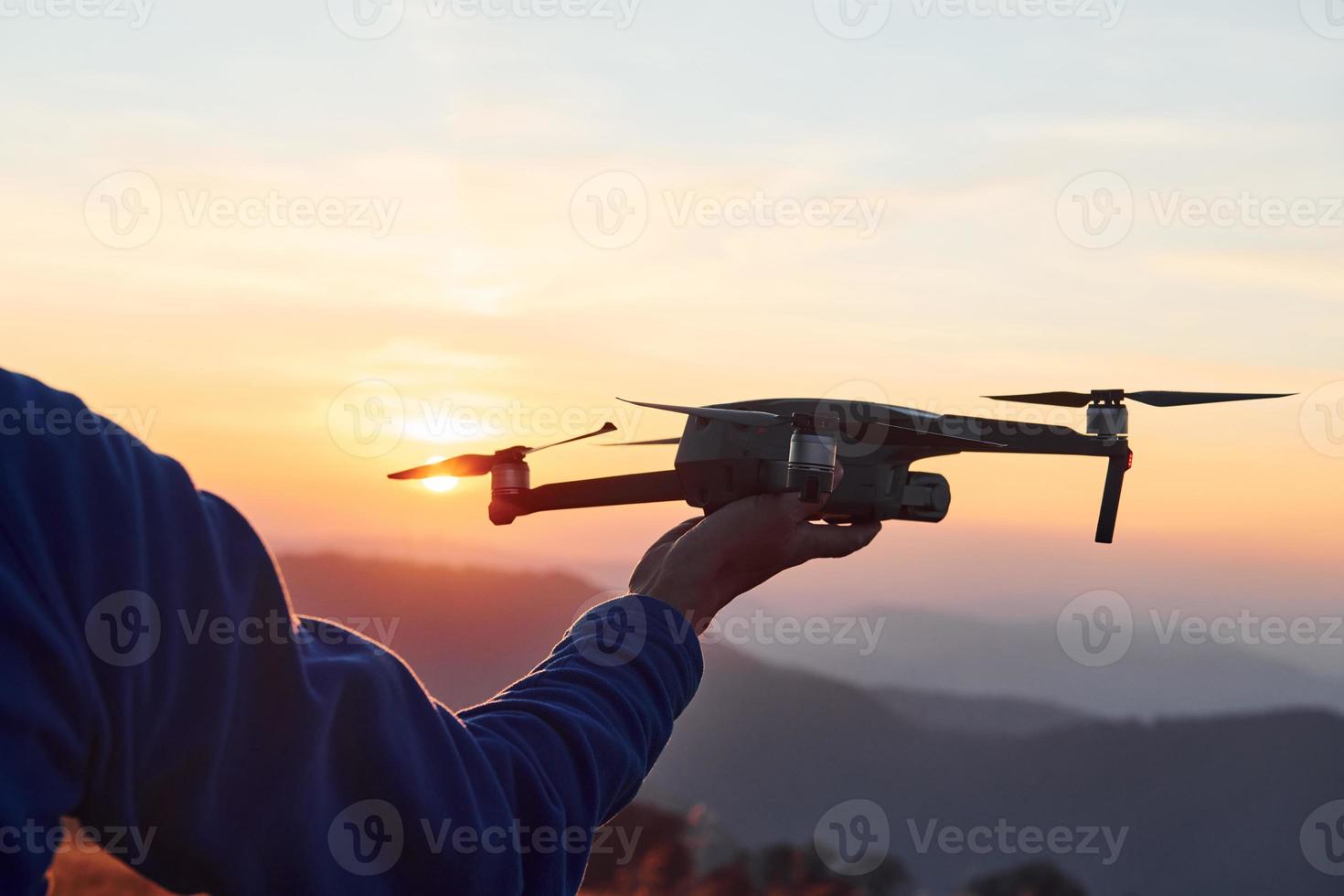 Man standing in the autumn field and holds drone in hand. Beautiful sunrise. Majestic landscape of mountains far away photo