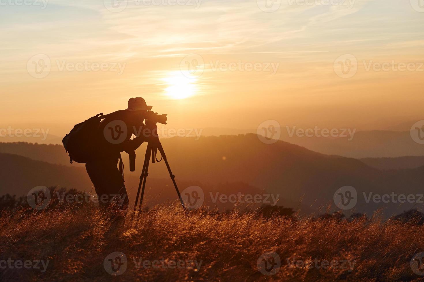 fotógrafo masculino de pie y trabajando en el majestuoso paisaje de árboles y montañas de otoño en el horizonte foto