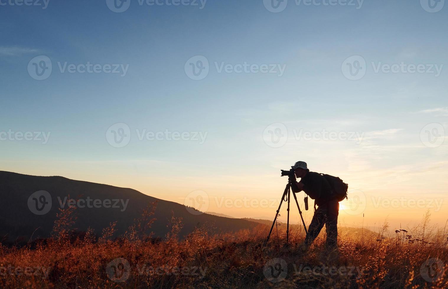 fotógrafo masculino de pie y trabajando en el majestuoso paisaje de árboles y montañas de otoño en el horizonte foto