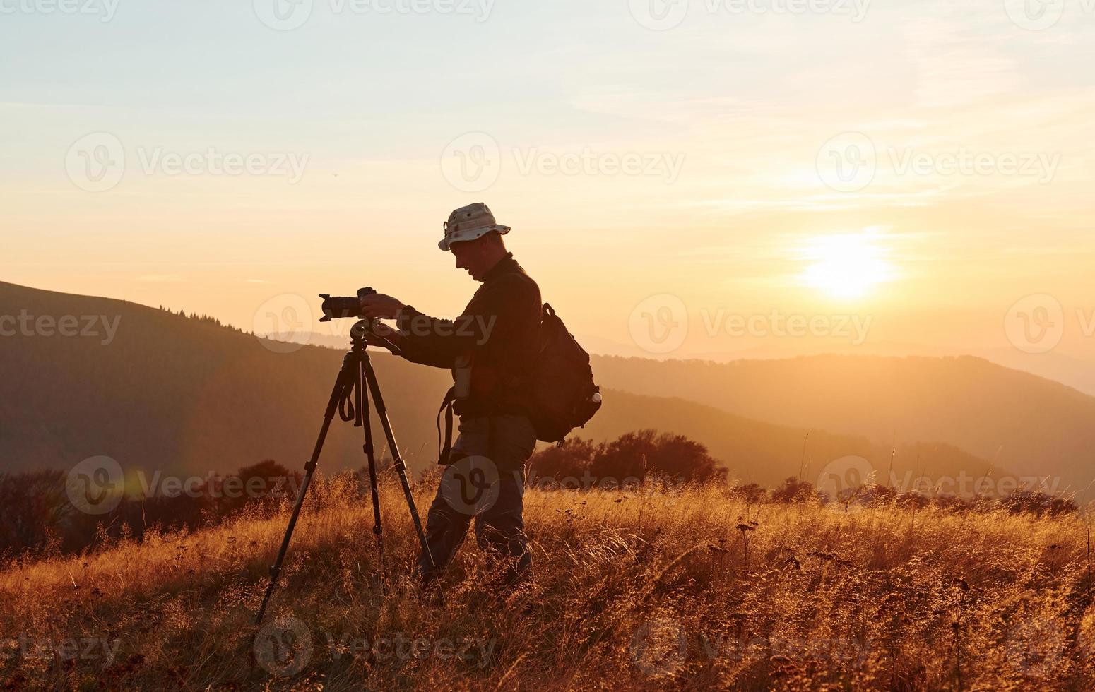 Male photographer standing and working at majestic landscape of autumn trees and mountains by the horizon photo