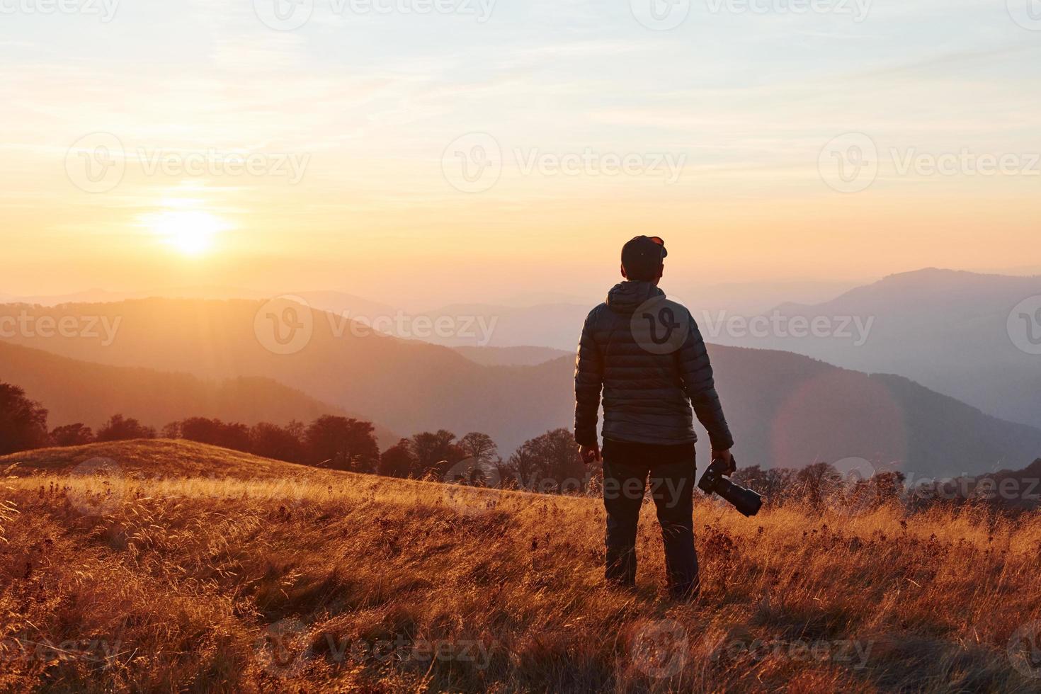 Male photographer standing and working at majestic landscape of autumn trees and mountains by the horizon photo