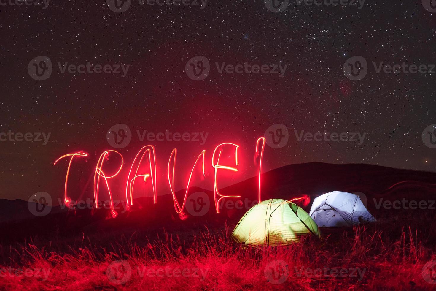 Red neon travel word. Two iluminated tents under stars at mountains at night photo