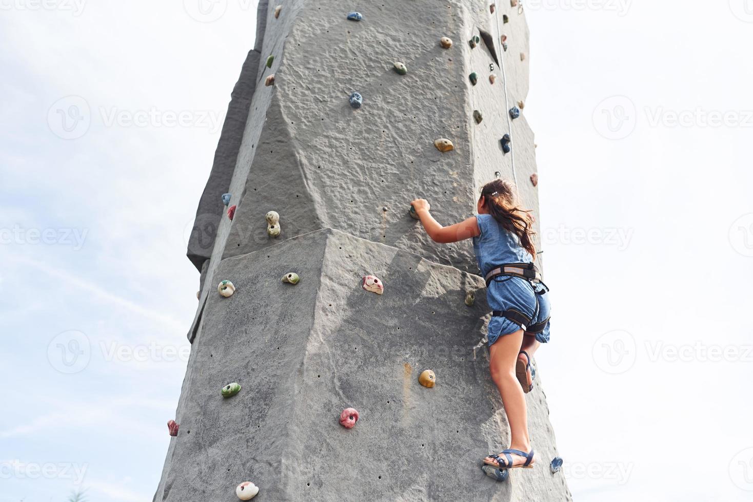 Little girl in casual blue clothes training rock climbing outdoors photo