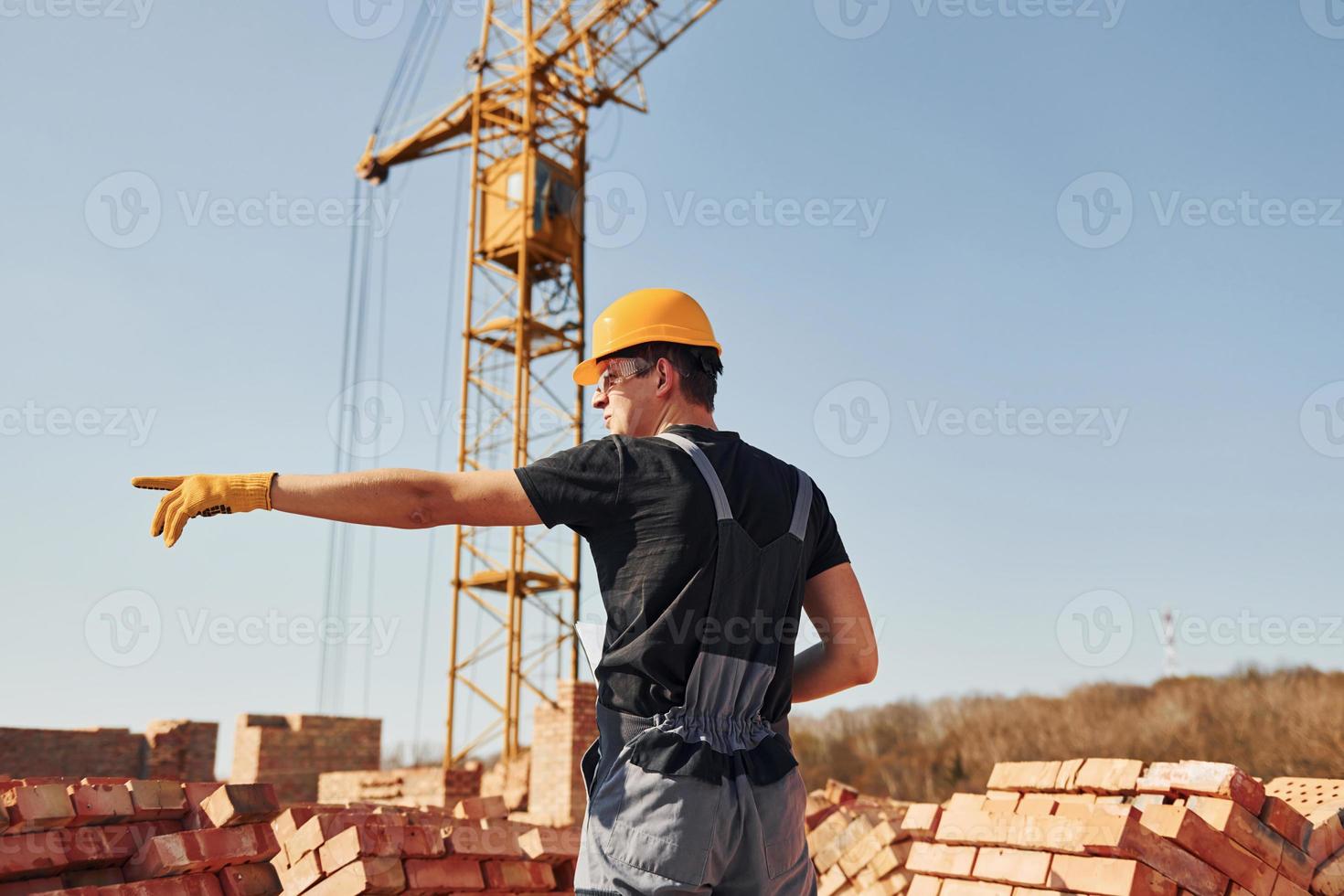 Shows gestures and talks. Construction worker in uniform and safety equipment have job on building photo