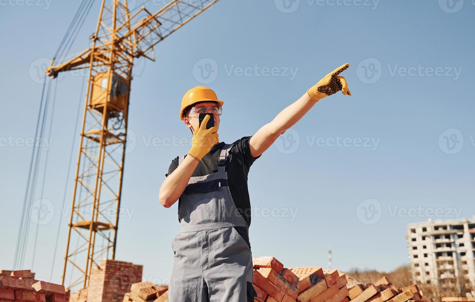 Talking by phone. Construction worker in uniform and safety equipment have job on building photo