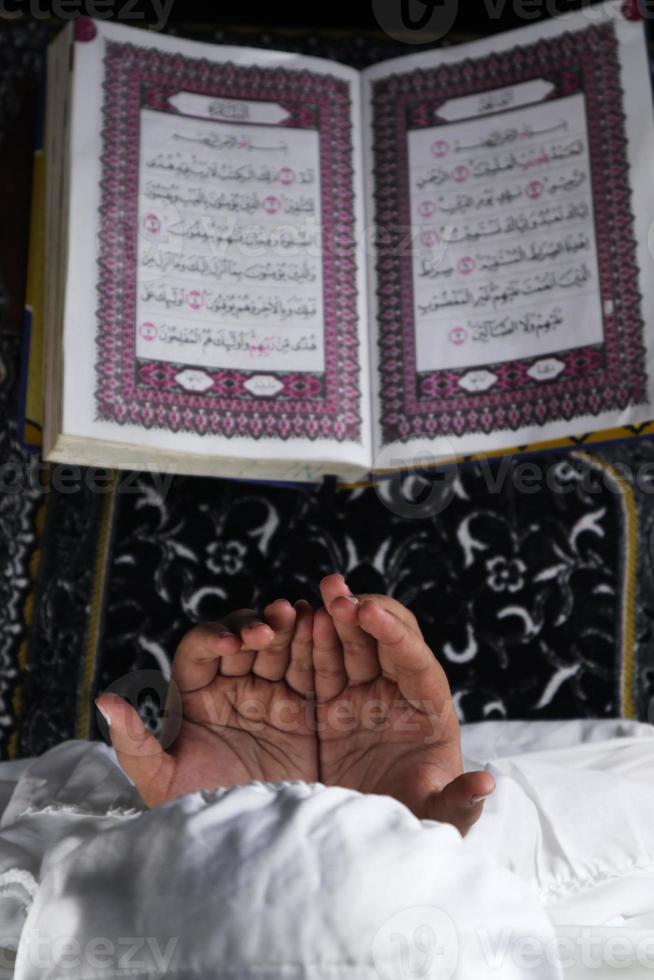 mano de niño rezando con las manos levantadas contra el fondo del corán. concepto islámico foto