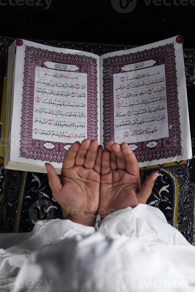 child hand praying with raised hands against the Quran background. Islamic concept photo