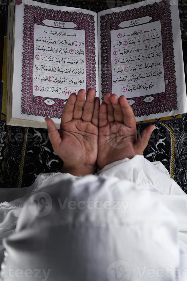 child hand praying with raised hands against the Quran background. Islamic concept photo