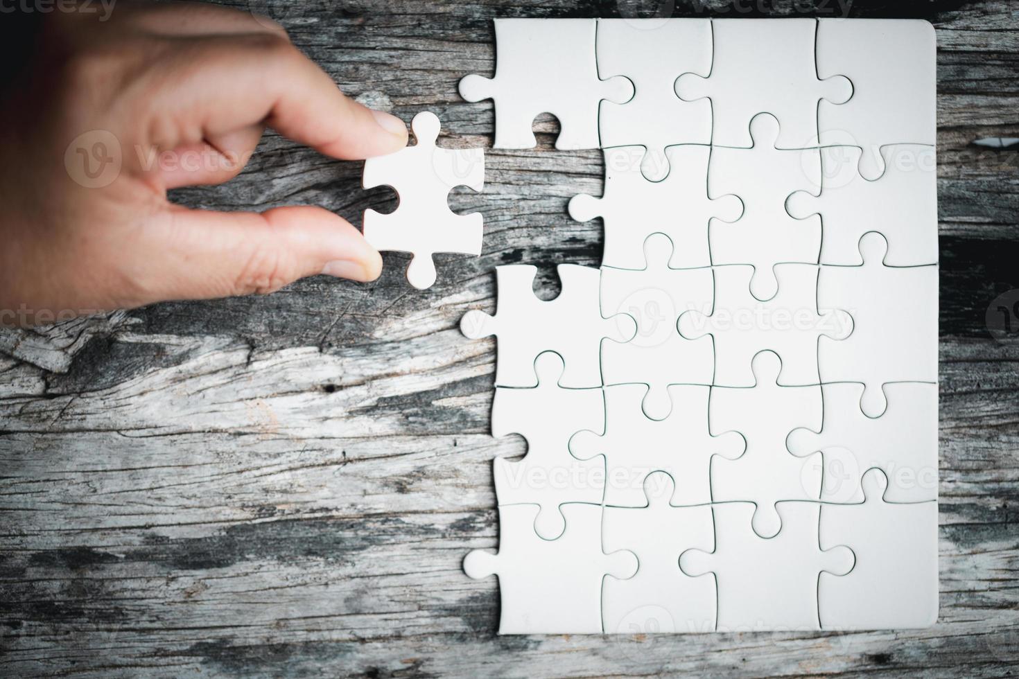 Pieces of jigsaw puzzle in woman's hands. White details of jigsaw puzzle piece on wooden background. Concept of working together as a business team. The idea of getting involved, working for success. photo