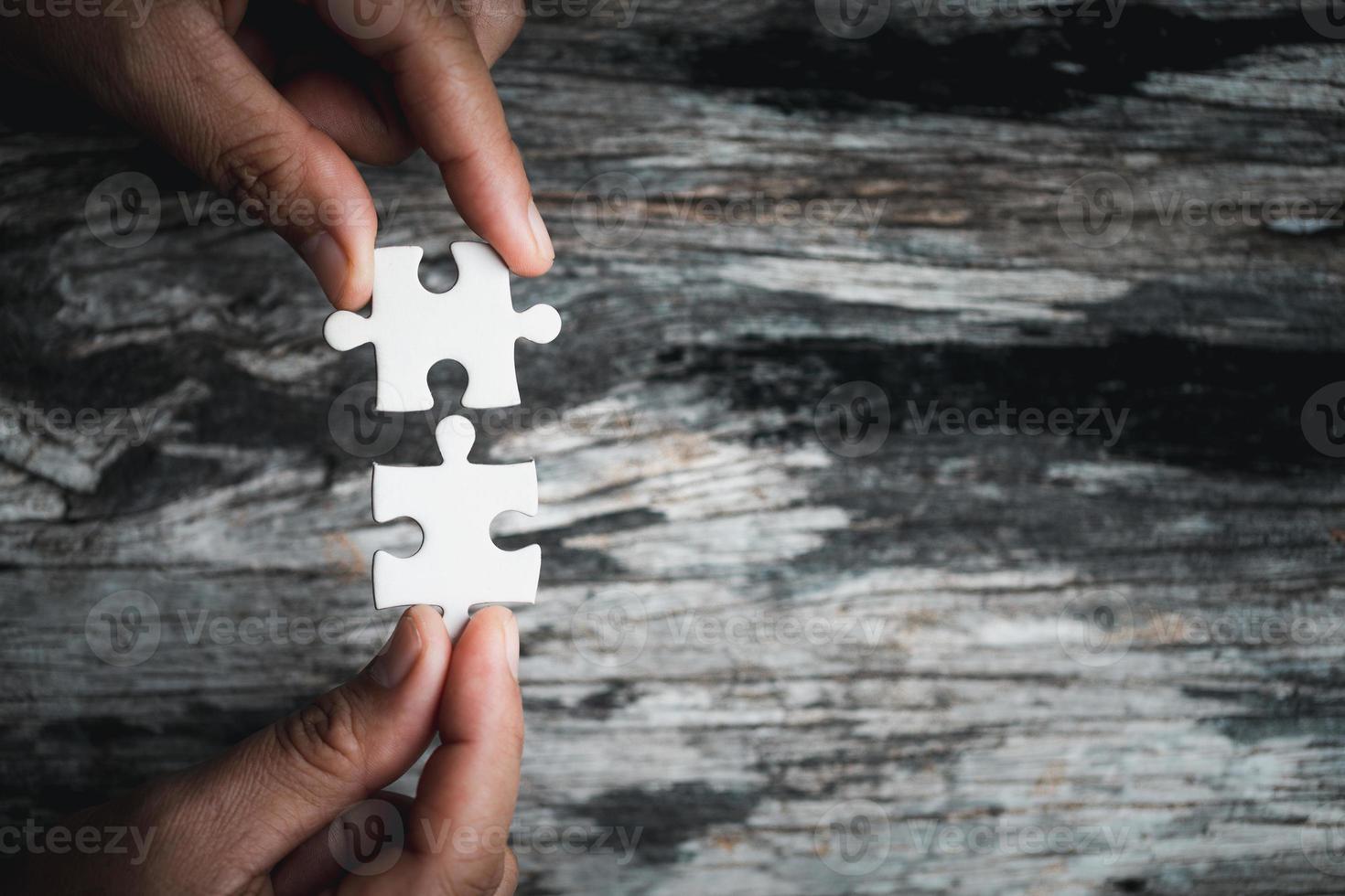 Pieces of jigsaw puzzle in woman's hands. White details of jigsaw puzzle piece on wooden background. Concept of working together as a business team. The idea of getting involved, working for success. photo