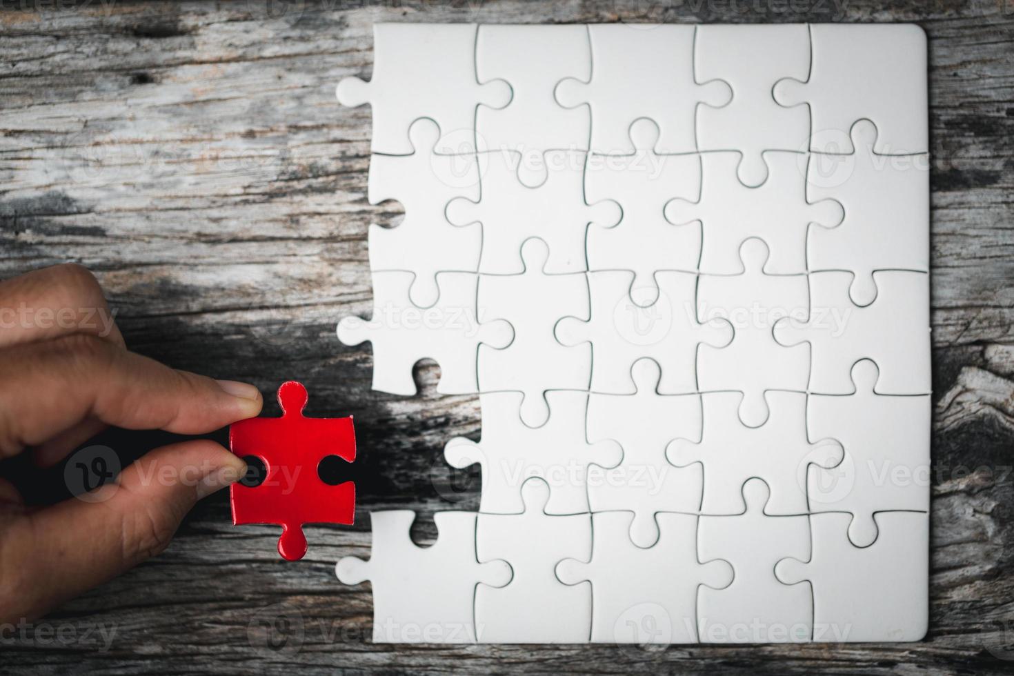 Pieces of jigsaw puzzle in woman's hands. White details of jigsaw puzzle piece on wooden background. Concept of working together as a business team. The idea of getting involved, working for success. photo