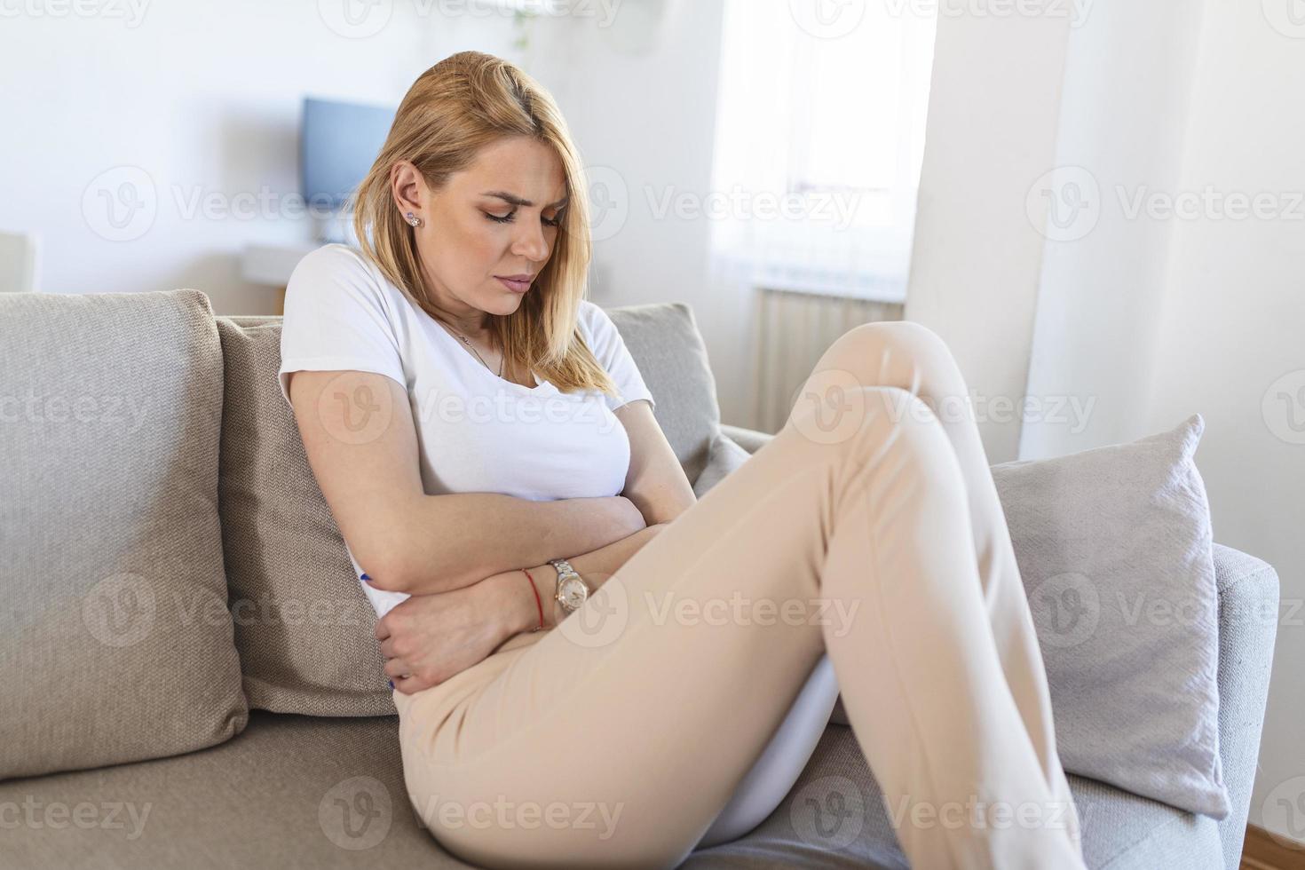 Young beautiful woman having painful stomachache. Woman with menstrual pain is holding her aching belly - body pain concept. woman having abdominal pain, upset stomach or menstrual cramps. photo