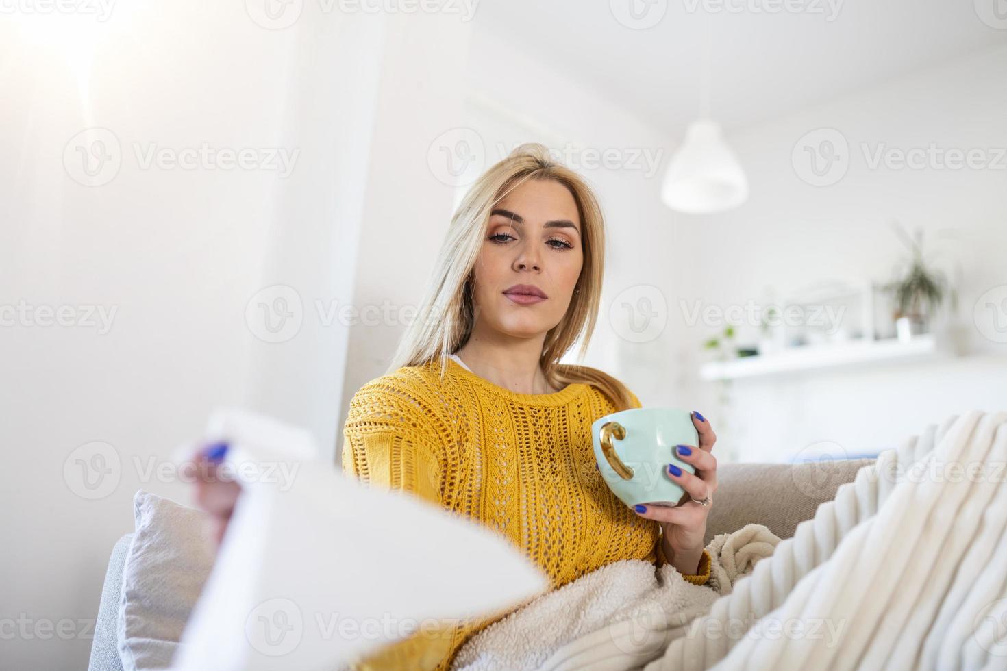 Sick attractive young woman has a cold and drinks hot tea upset young blonde in a sweater and blanket feels bad, cold, nausea, chills. photo