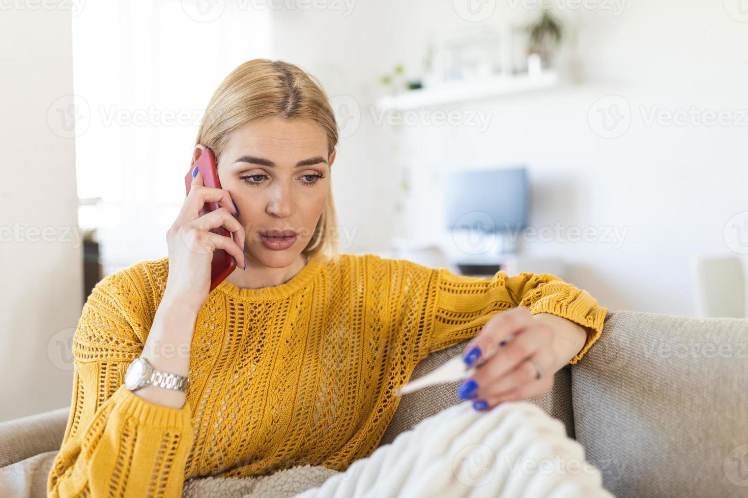 Young woman is looking at the thermometer. She has fever, calling her doctor. Beautiful woman with symptoms called covid-19 emergency number to report her medical conditions photo