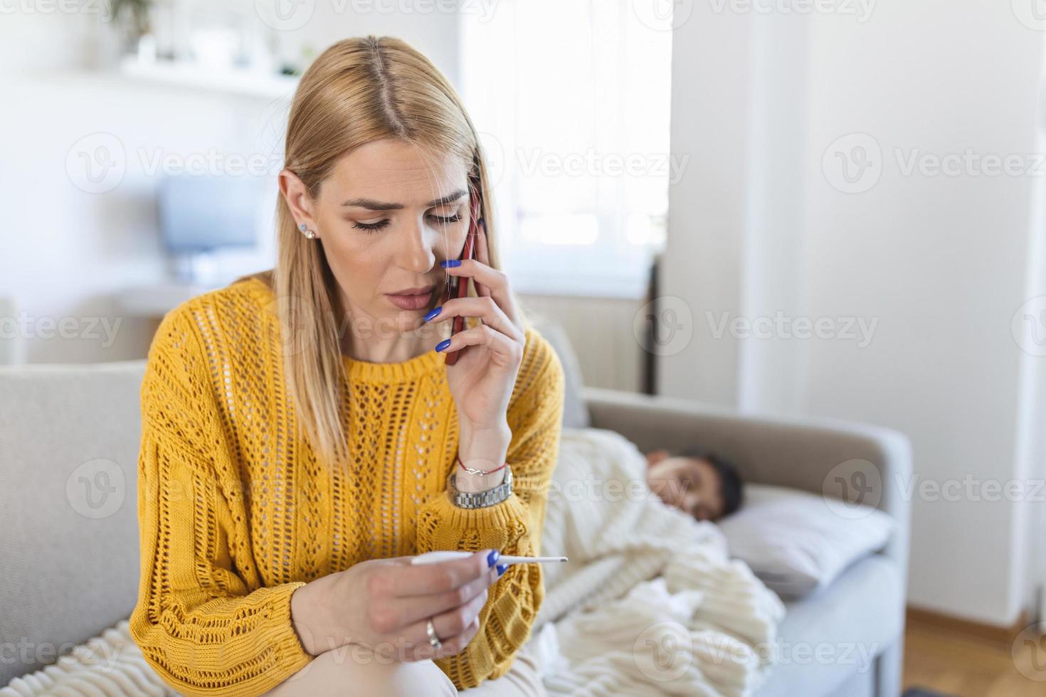 Sick boy with thermometer laying in bed and mother hand taking temperature. Mother checking temperature of her sick son and calling a doctor. Sick child with fever and illness in bed. photo