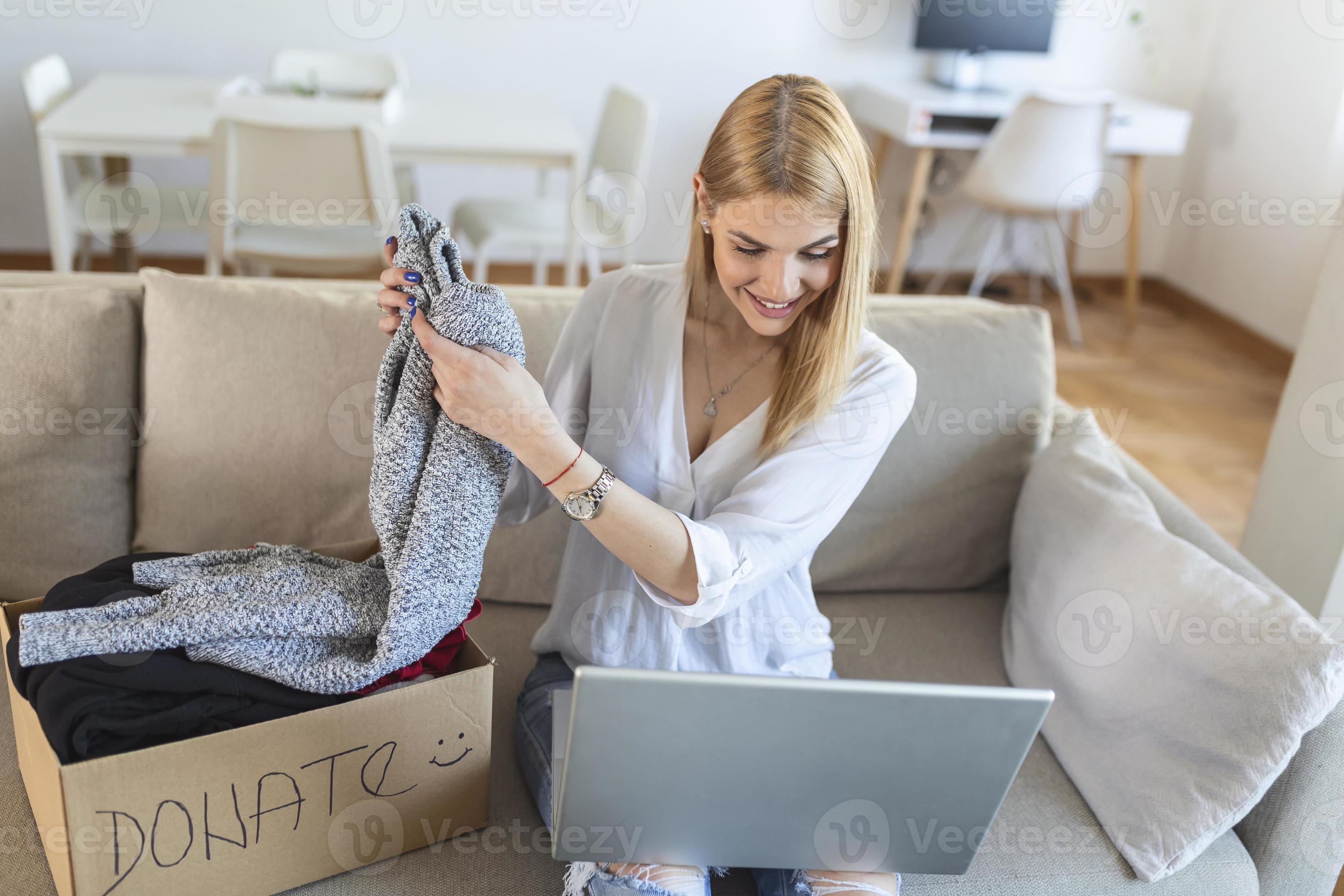 Happy blond young woman sit on couch stuck clothes in donation box at