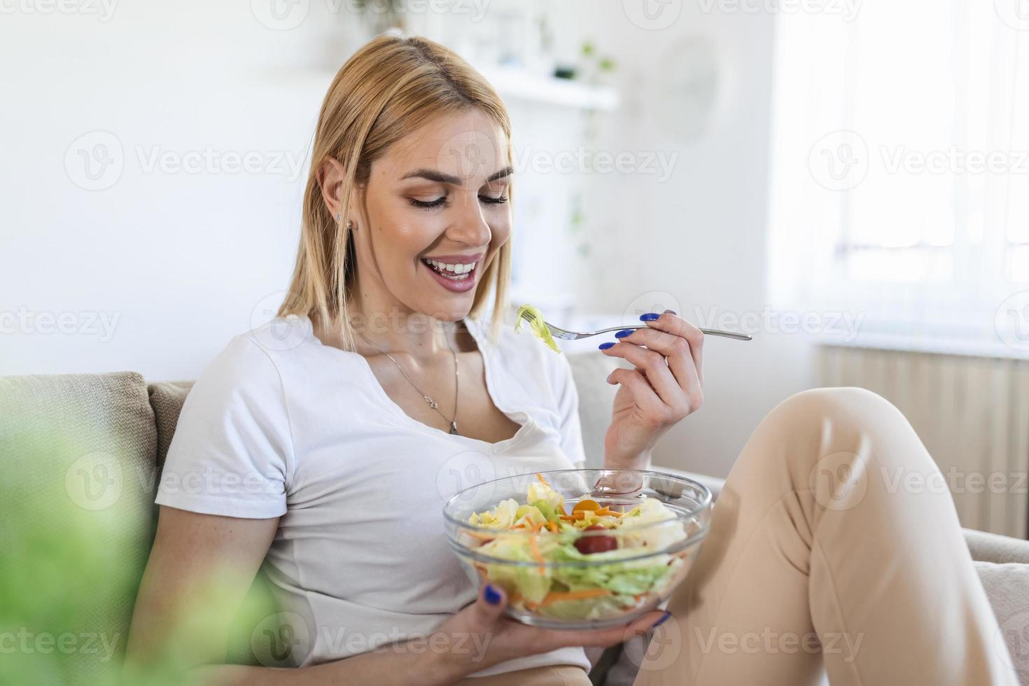 mujer joven y feliz comiendo ensalada saludable sentada en el sofá con ingredientes verdes frescos. mujer comiendo ensalada de verduras. dieta saludable foto