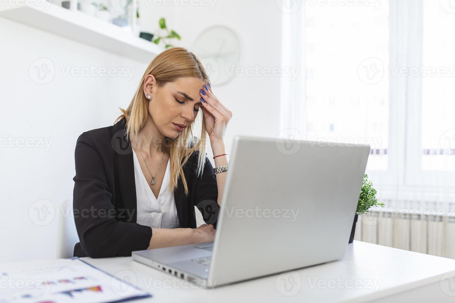 Feeling exhausted. Frustrated young woman looking exhausted while sitting at her working place and carrying her glasses in hand photo