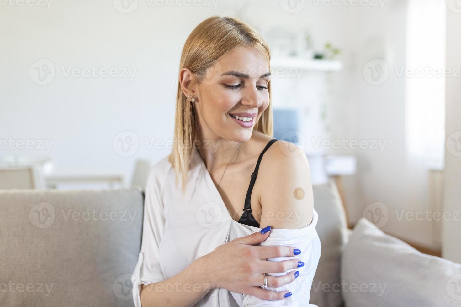 Portrait of a female smiling after getting a vaccine. Woman holding down her shirt sleeve and showing her arm with bandage after receiving vaccination. photo