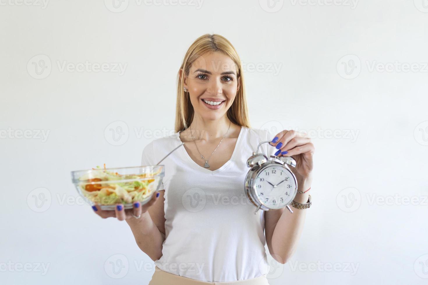 Young woman holding clock and Healthy food of salad Intermittent fasting concept. Time to lose weight , eating control or time to diet concept. photo