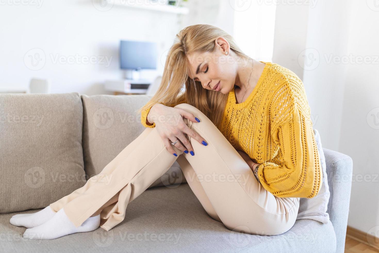 Woman in painful expression holding hands against belly suffering menstrual period pain, lying sad on home bed, having tummy cramp in female health concept photo