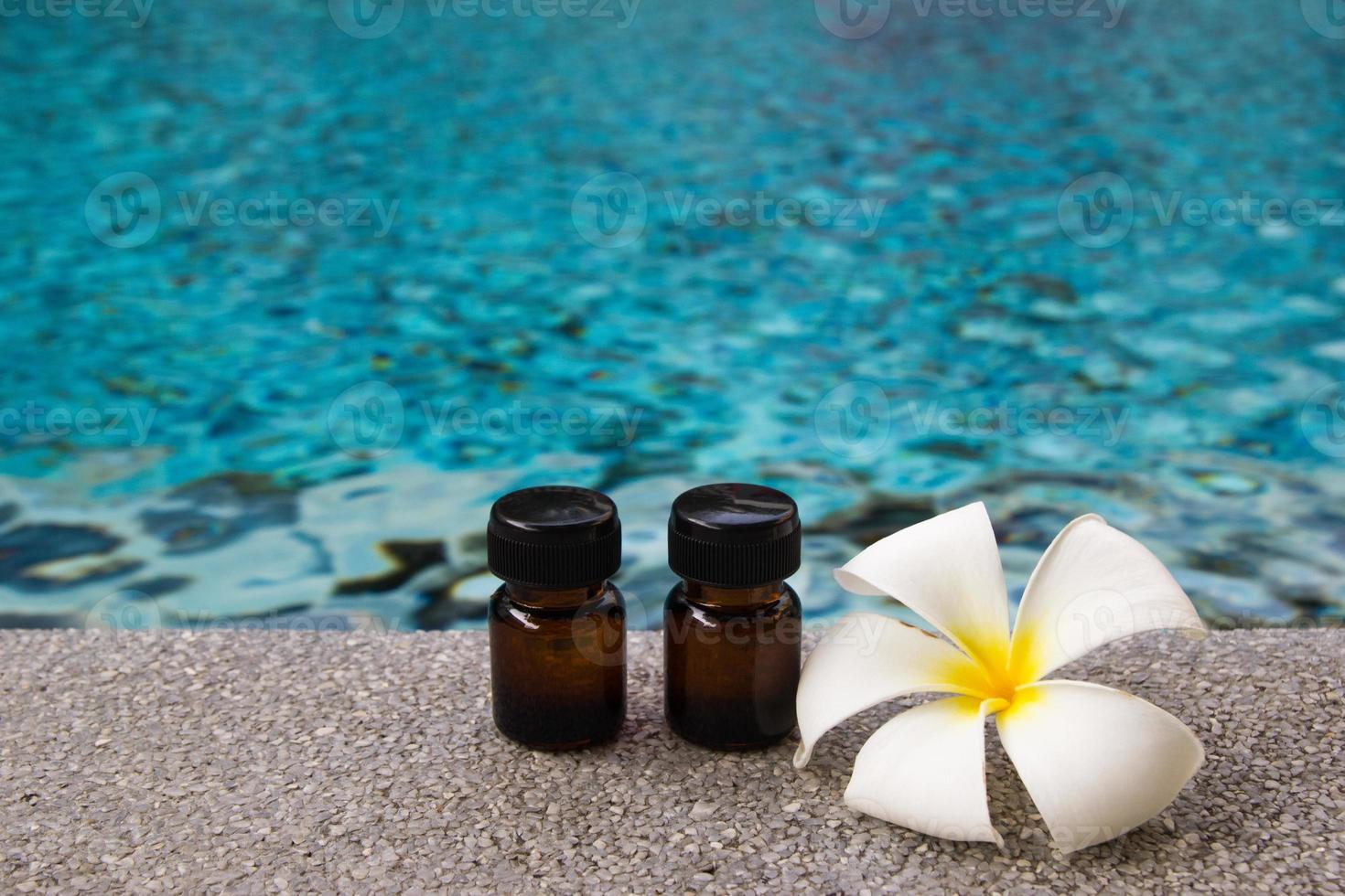 Two bottles of aroma essential oil and flower of frangipani on the swimming pool background for spa theme. photo