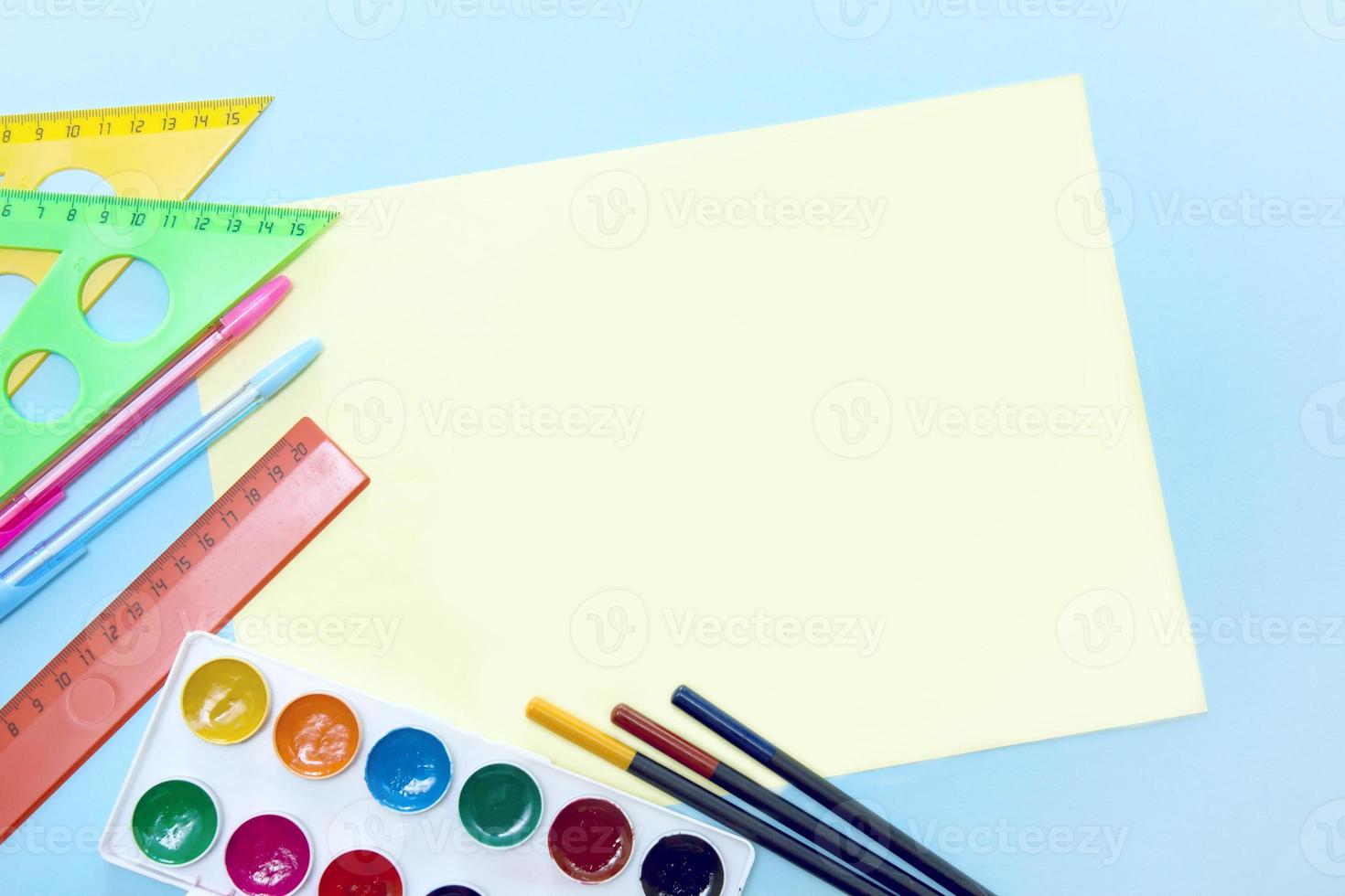 empty yellow sheet for text surrounded by school stationery accessories - watercolor, pencils, ruler, pens, triangle with copy space photo