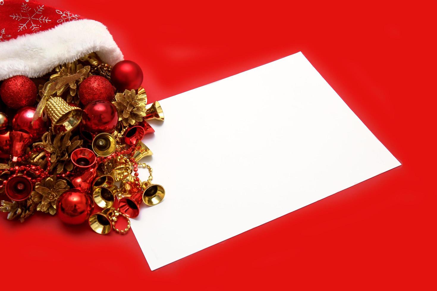 los juguetes navideños se derraman del sombrero de santa, junto a una sábana blanca vacía sobre un fondo rojo, copyspace, contenido navideño foto