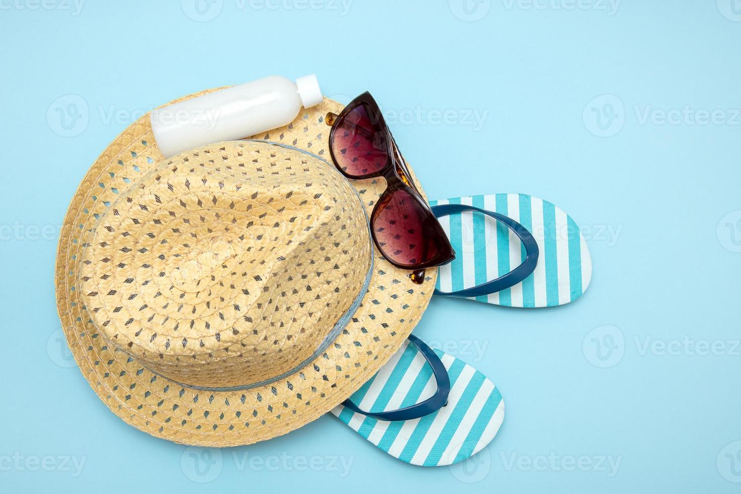 straw hat, sunglasses striped flip flops sun cream on blue background, summer background photo