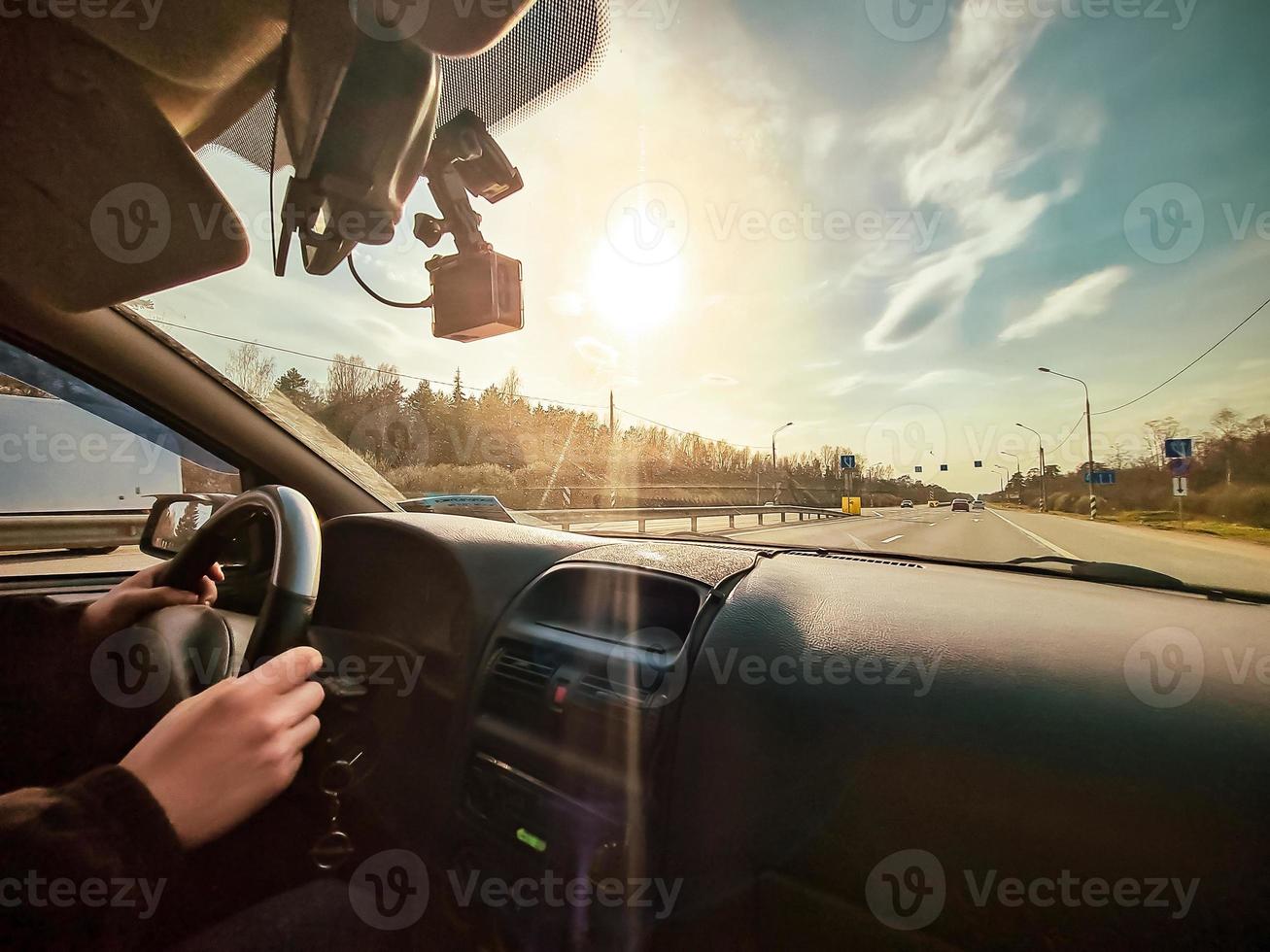 View from the car to the road in sun. The driver drives the vehicle. Hands on the wheel. photo