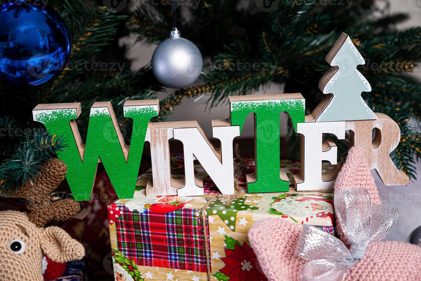 The inscription winter from a tree on a New Year's. On the spruce branches against the background of a snow cover are New Year's blue, white balls with spruce cones and a box with a gift. Christmas photo