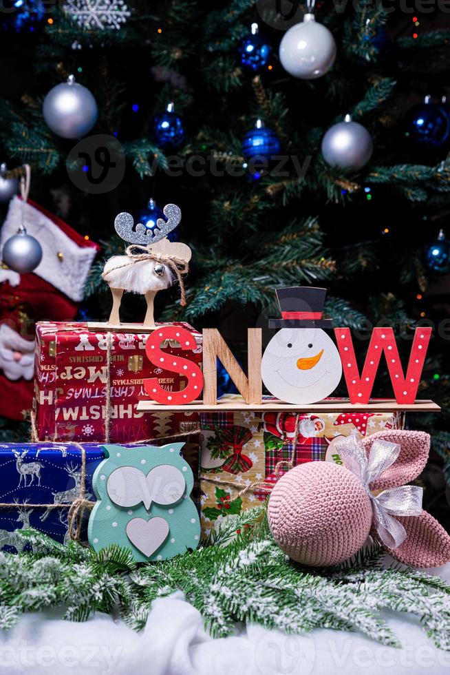 The inscription snow from a tree on a New Year's. On the spruce branches against the background of a snow cover are New Year's blue, white balls with spruce cones and a box with a gift. Christmas photo