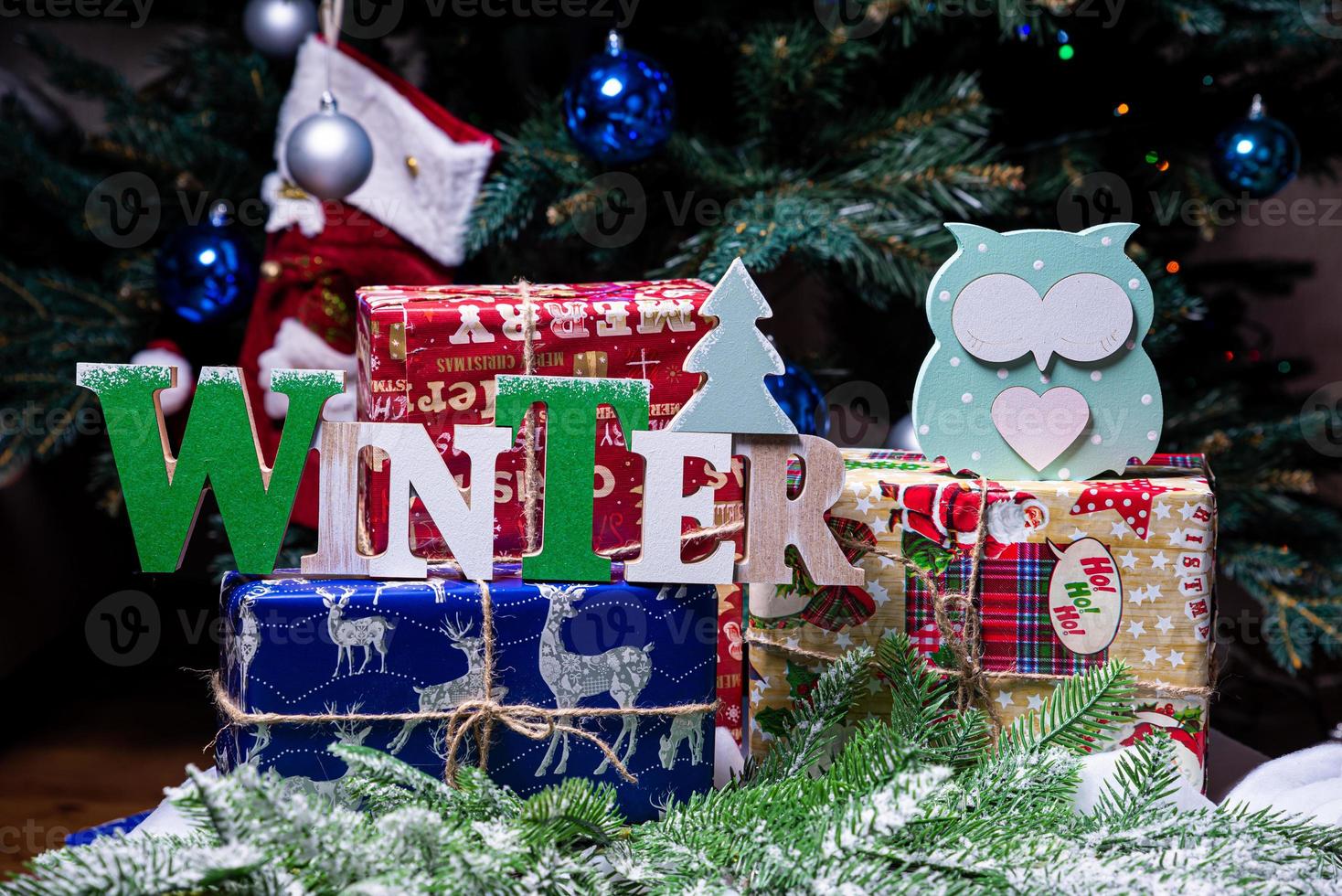 The inscription winter from a tree on a New Year's. On the spruce branches against the background of a snow cover are New Year's blue, white balls with spruce cones and a box with a gift. Christmas photo